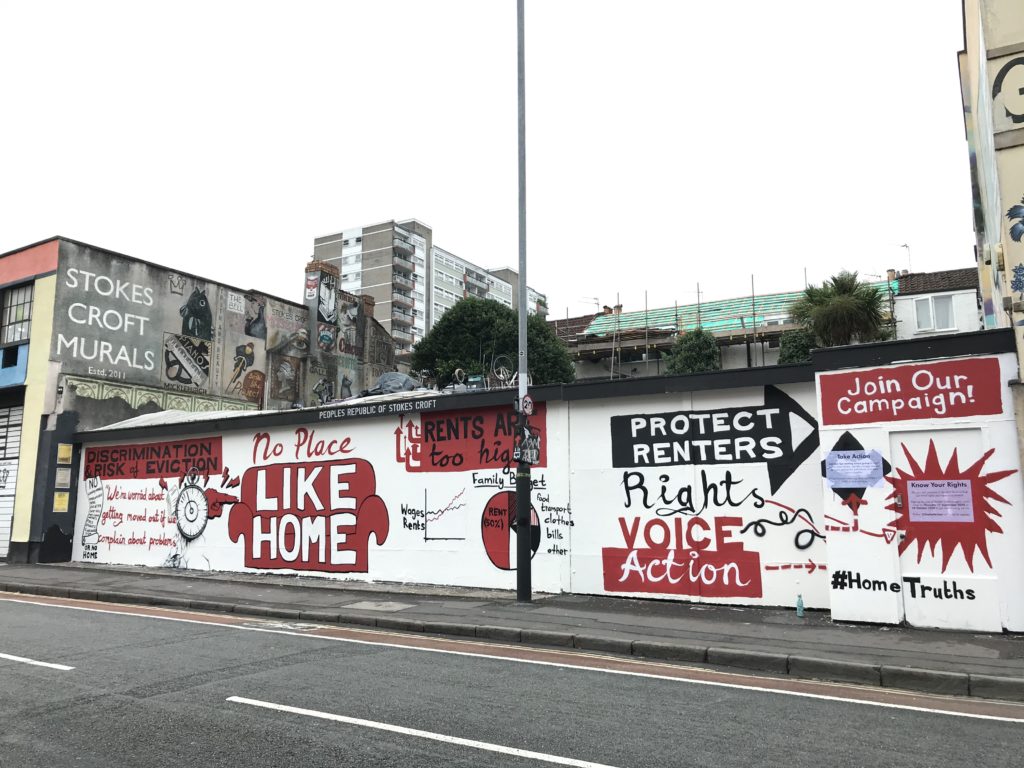 A red and white mural on a wall exposing the realities of private renting in Bristol