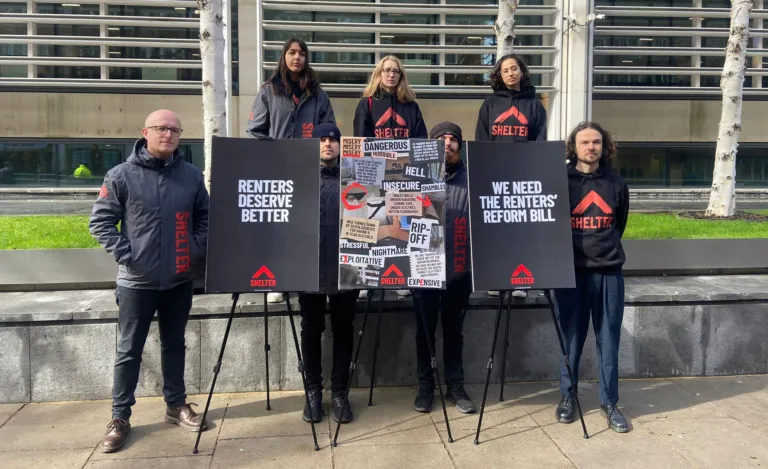 A group of people wearing black hoodies with the Shelter logo on, standing beside placards reading 'Renters deserve better' and 'We need the Renters' Reform Bill'.