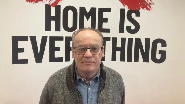 Martin, a Shelter volunteer, stands in front of a sign reading 'Home is everything'