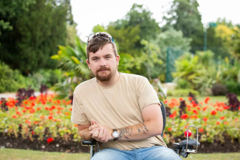 A man in a wheelchair in front of a garden in a park