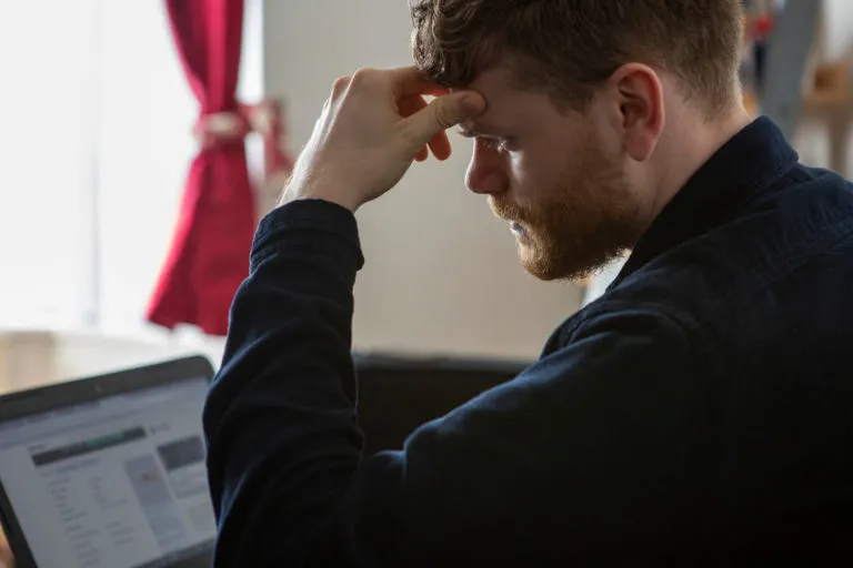 Man looking at laptop with head in his hands