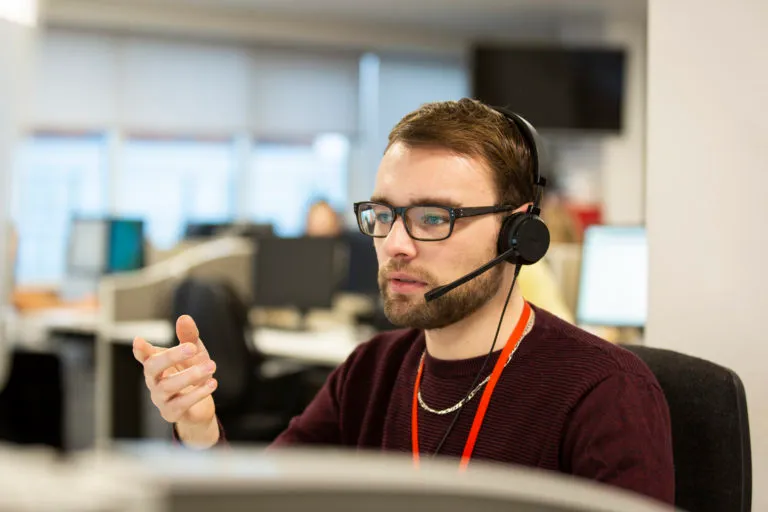 A male Shelter helpline adviser, wearing a headset and in the middle of a call