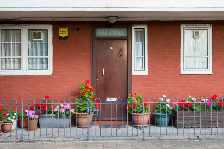 Front door of an orange house, surrounded by bright flowers in pots