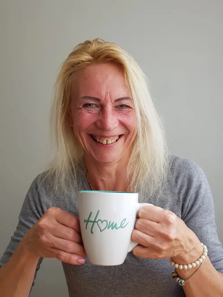 Kate smiling, holding a mug with the word &#x27;home&#x27; on it.