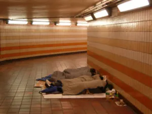 People sleeping in an underpass under a blanket.