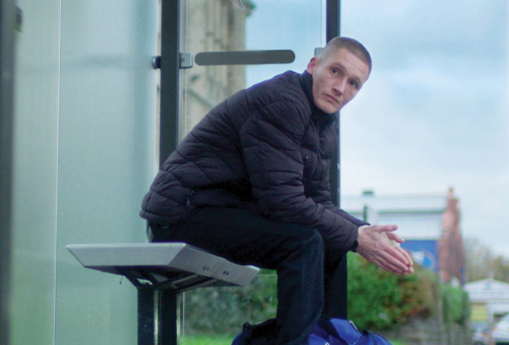 Rhys, a former rough sleeper who now has a safe home thanks to support from Shelter, sits at a bus stop
