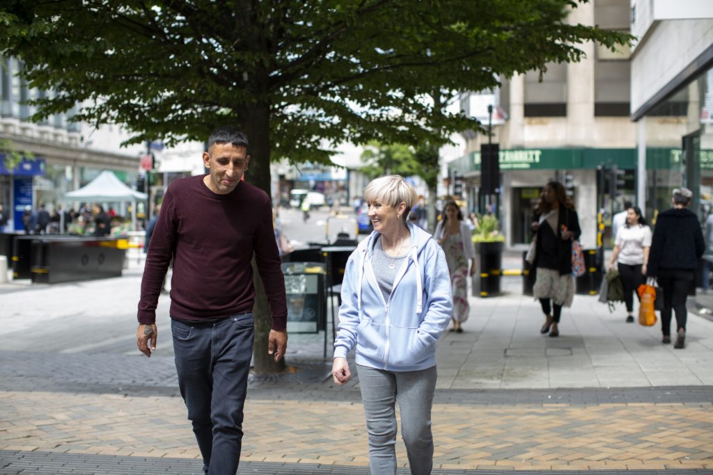 Paddy Burke and Shelter Peer Mentor Colette Carter walking through a town centre, smiling