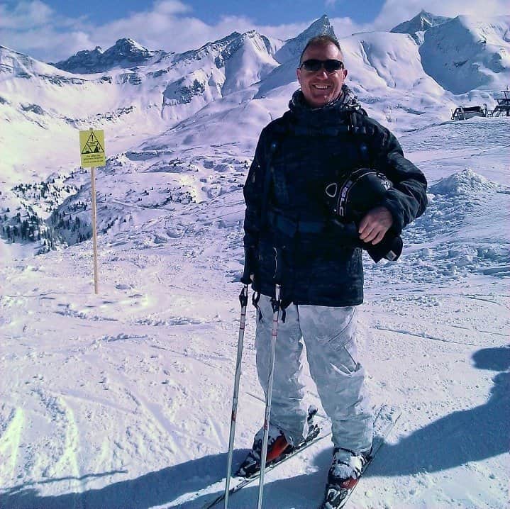 Kevin in ski wear, smiling on top of a ski slope