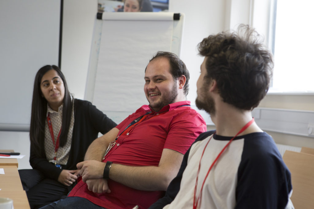 A woman and two men taking part in a meeting between Shelter staff and service users. They are smiling. 