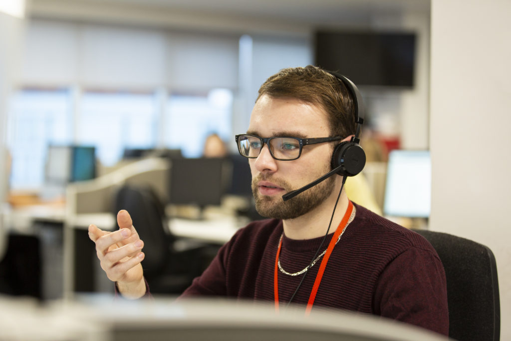 A male Shelter helpline adviser, wearing a headset and in the middle of a call