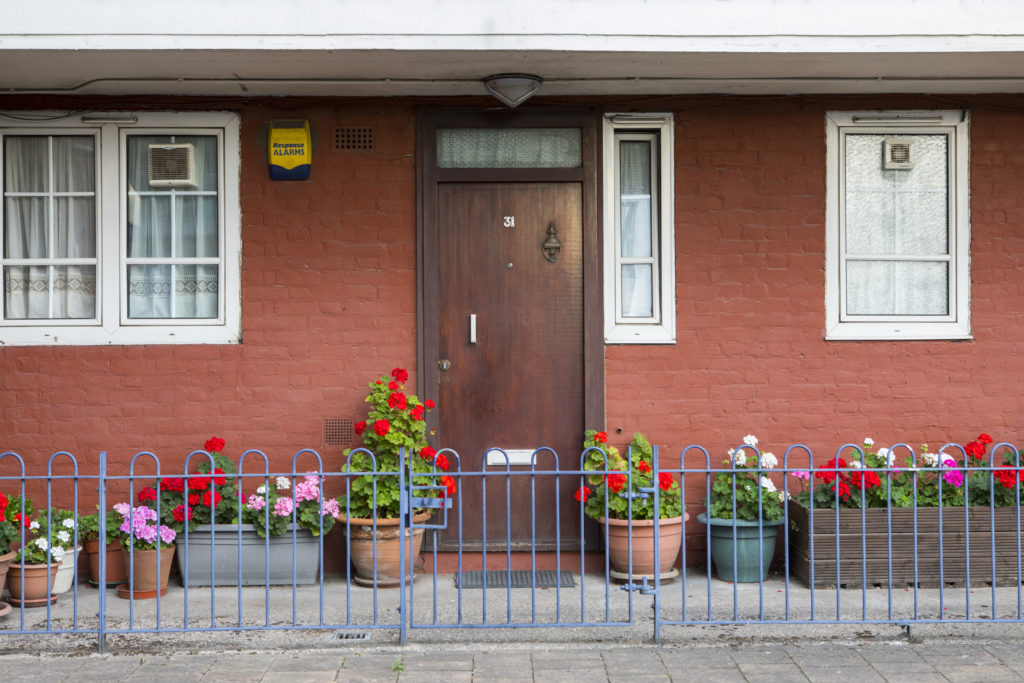Front door of an orange house, surrounded by bright flowers in pots