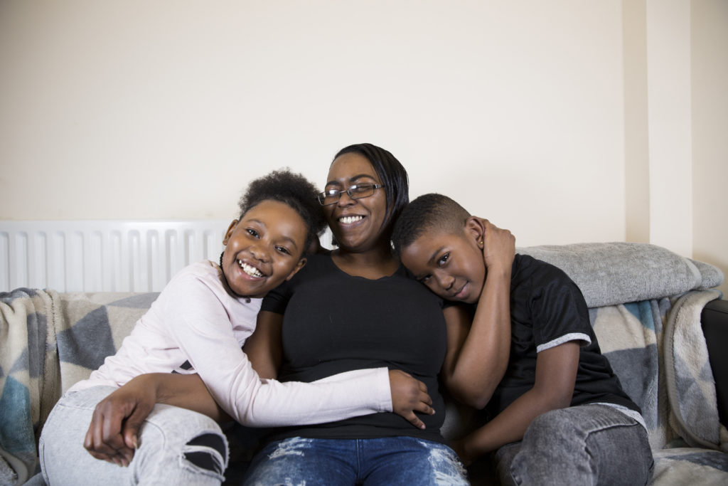 A woman sits on a sofa with children either side of her. They're cuddling and smiling