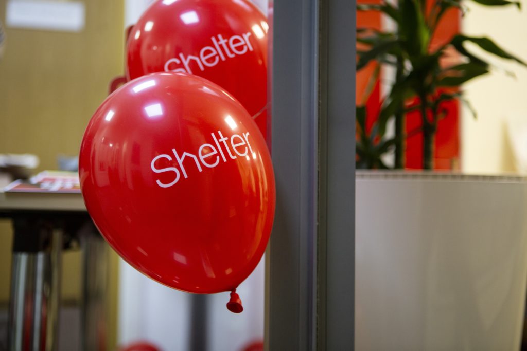 Two red balloons with the word Shelter on them, in an office