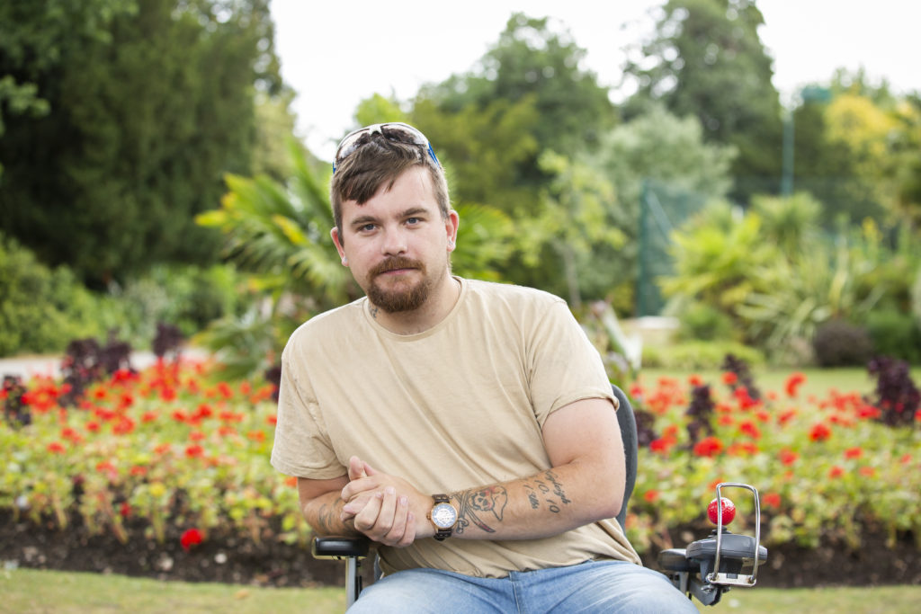A man in a wheelchair in front of a garden in a park