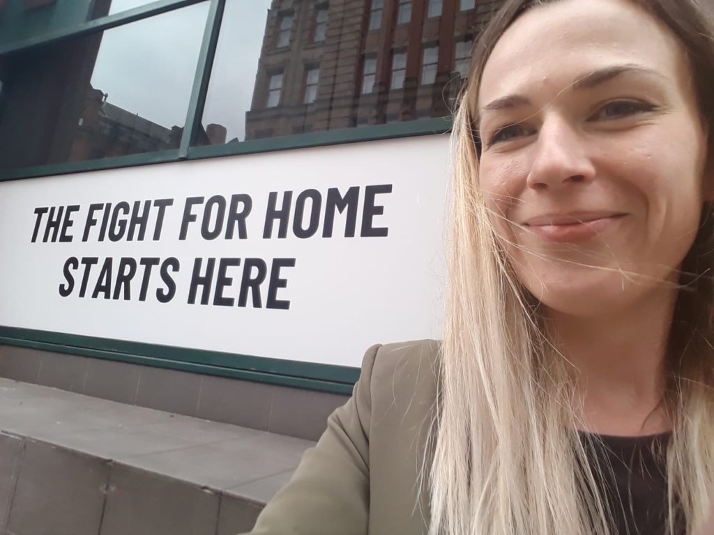 A woman with blonde hair standing next to a 'fight for home' sign