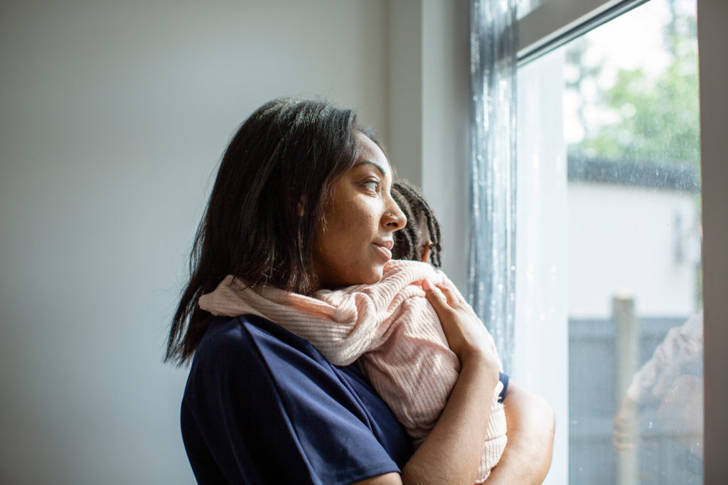 A woman holds her baby whilst looking out the window
