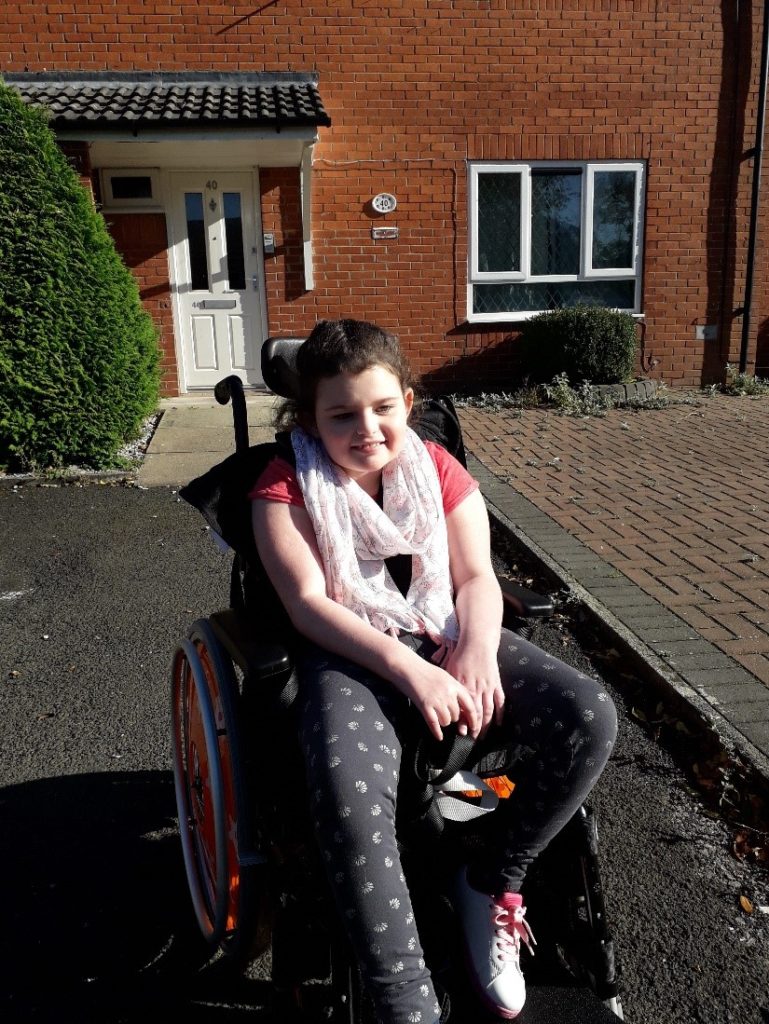 A girl in a wheelchair outside a house