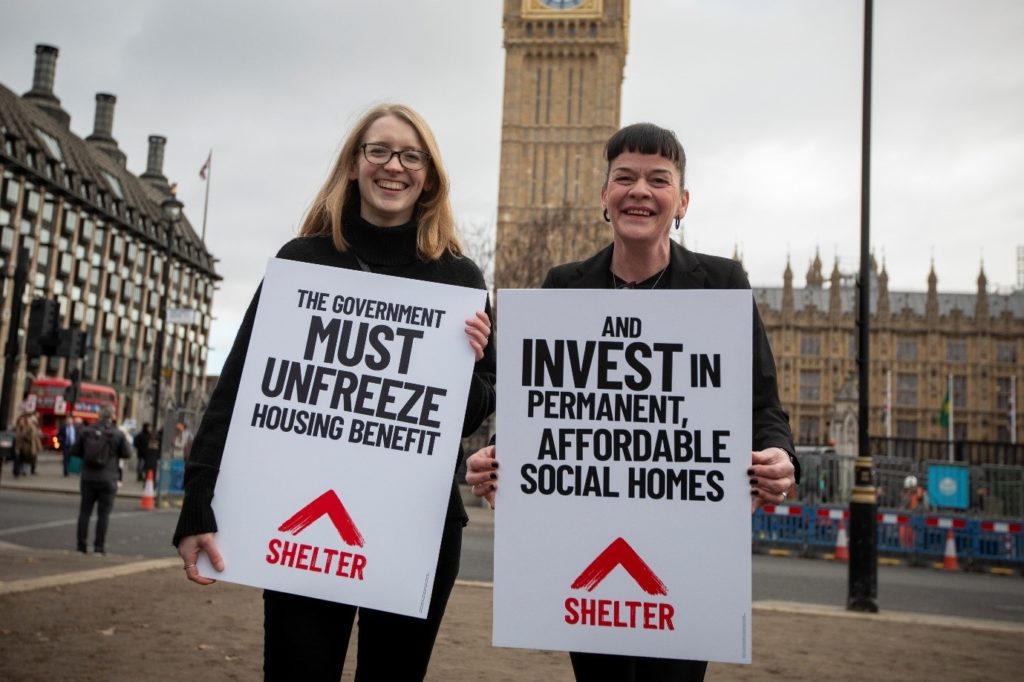 Two campaigners holding up signs about building social homes and unfreezing housing benefits in London