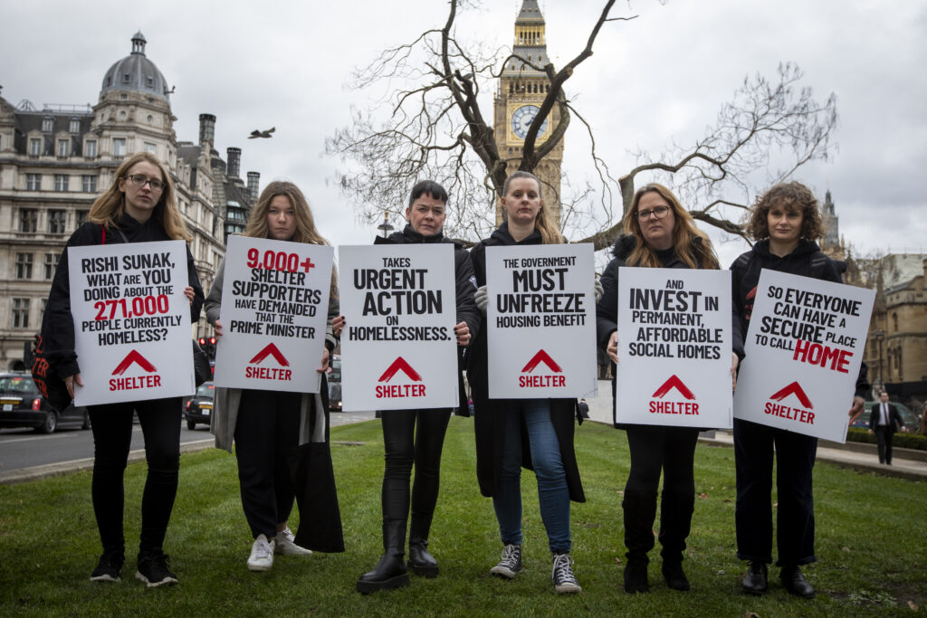 A group of campaigners stand in solidarity holding signs about the conditions relating to homelessness
