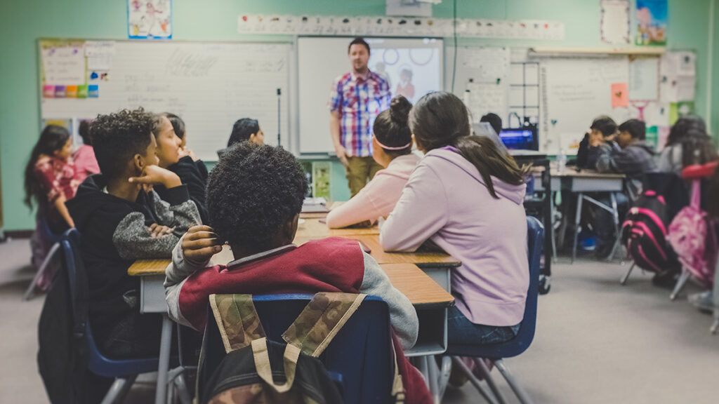 A teacher stands at the front of a classroom of students