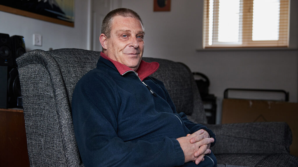 Dave Lockyer sits on a sofa at home