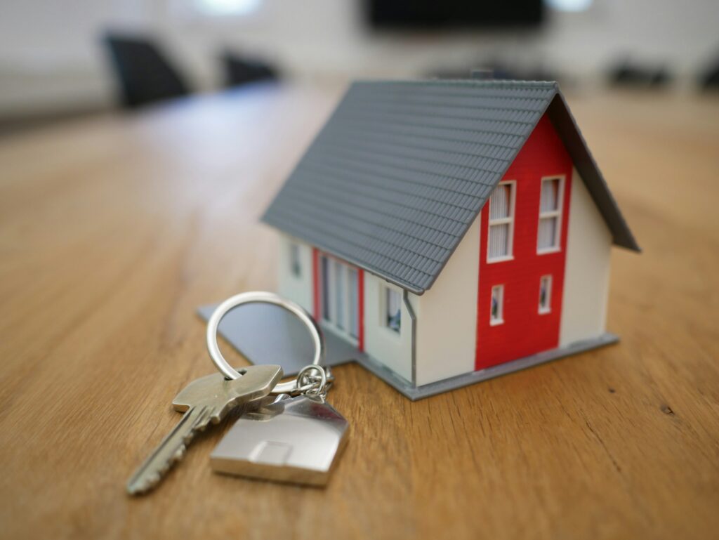 A small red and white model house on a table, next to a set of house keys