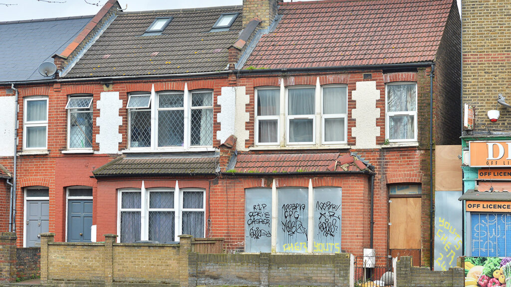A terrace with a boarded up derelict house next to a house where people are living